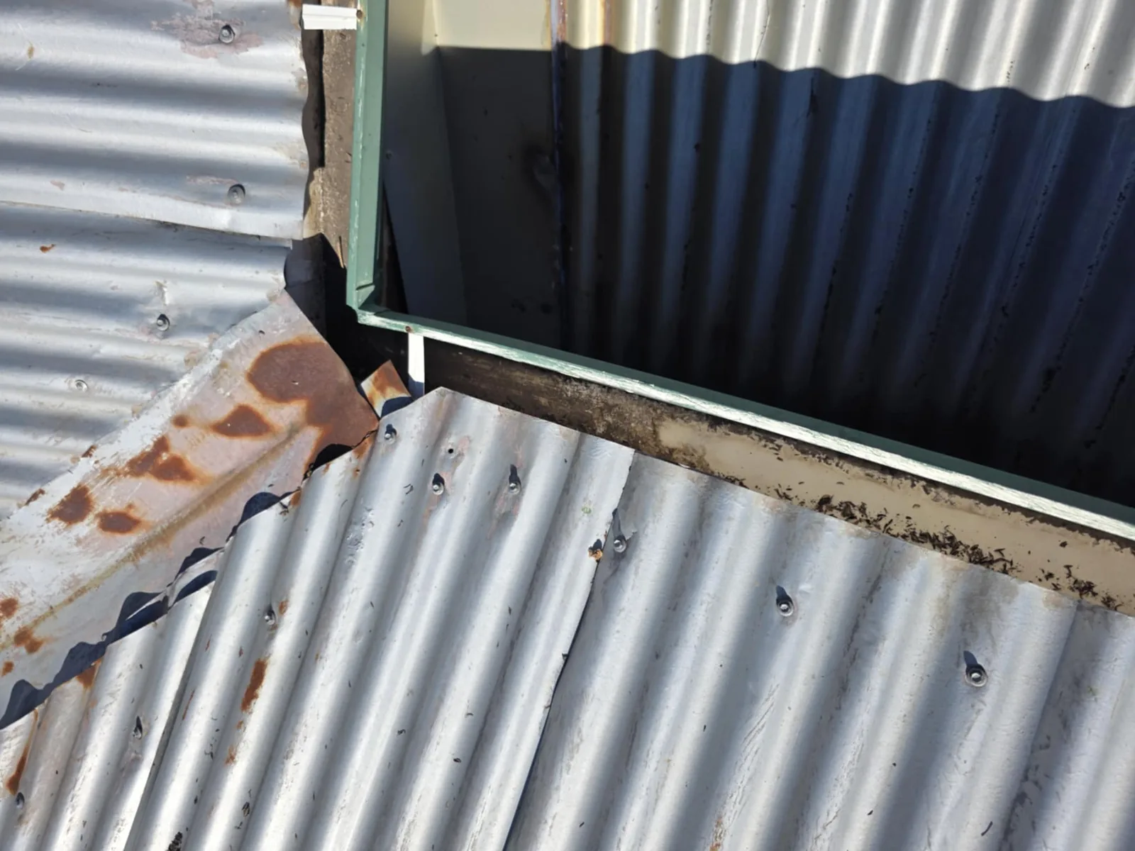 Damaged corrugated metal roof sheet edges at a junction before repair