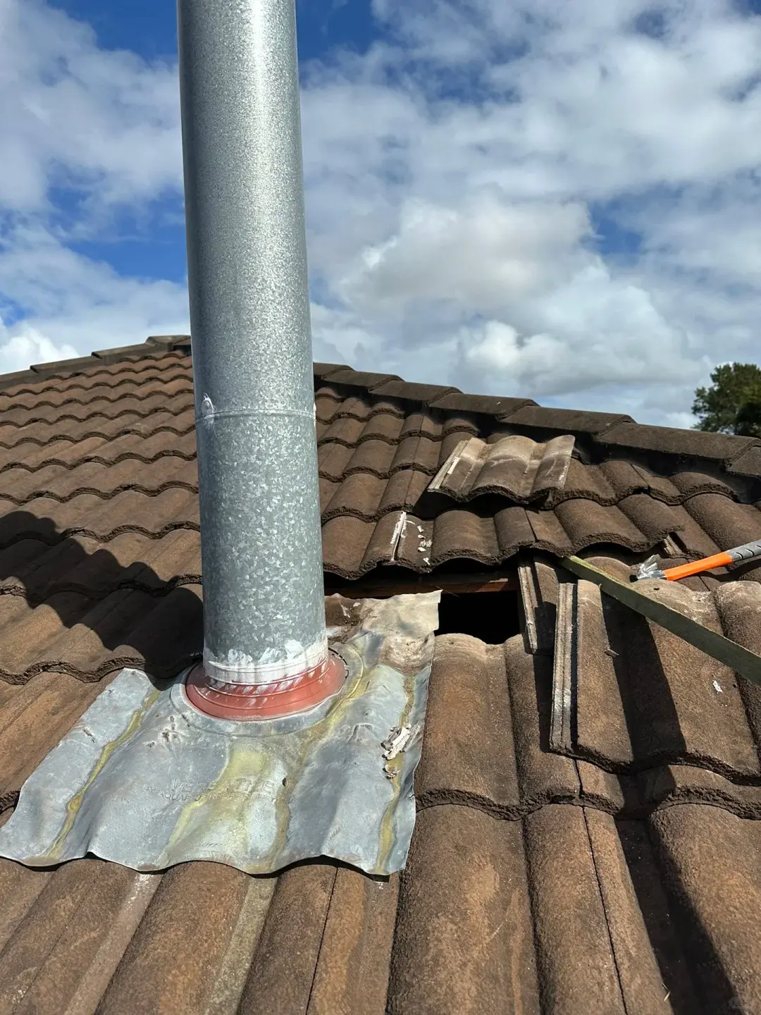 Lifted concrete roof tiles and exposed flashing around a flue penetration