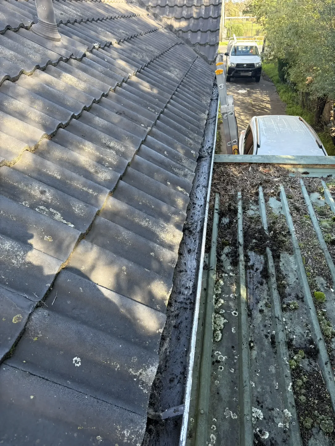 Debris collected in the gutter between tiled and metal roof sections before cleaning