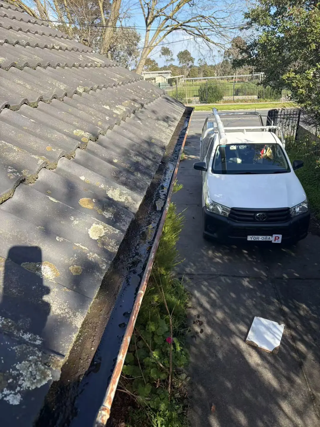 Long gutter run beside an older tile roof during clearing work