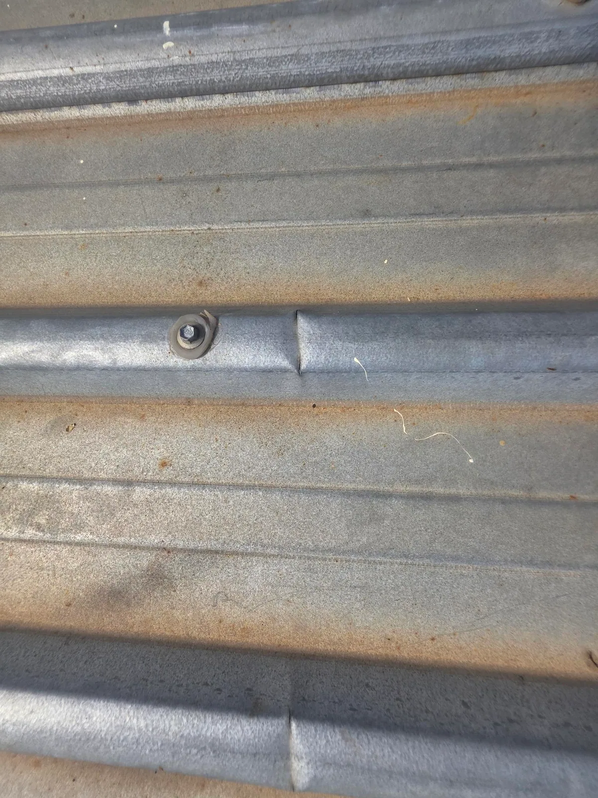 Close inspection view of a metal roof sheet fastener, seam and light surface spotting