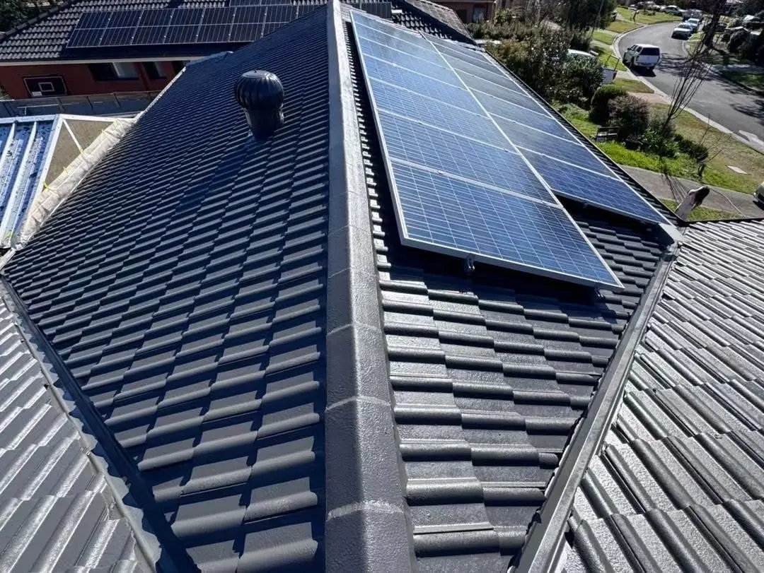 Completed dark-grey tile roof restoration beside a solar panel array